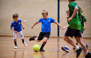 Young boy kicking a futsal ball on an indoor court